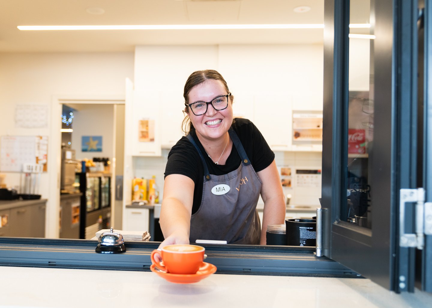 Girl wearing black glasses and black tshirt holding out hand with orange cup and saucer