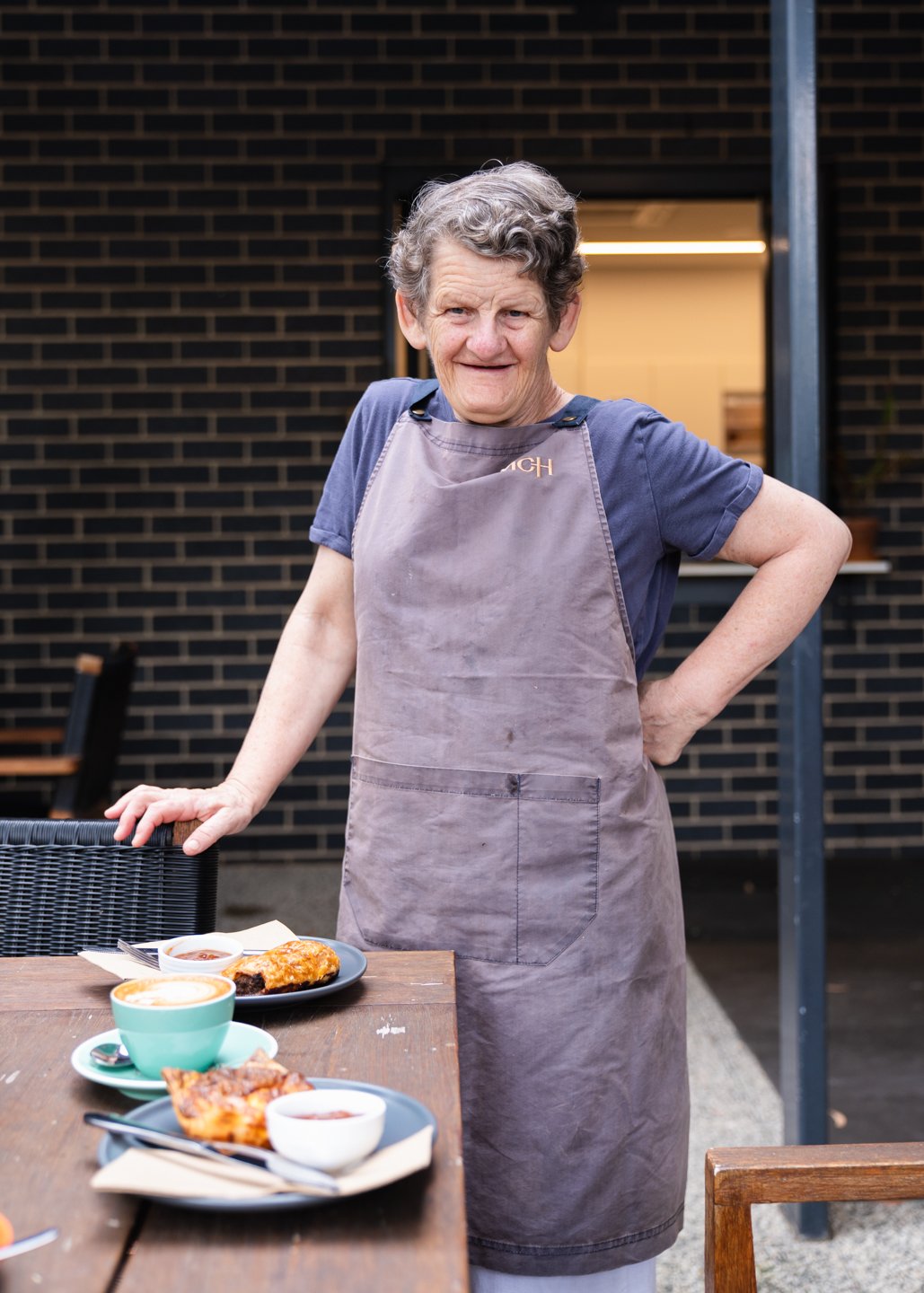 Person standing with arm on hip wearing grey apron