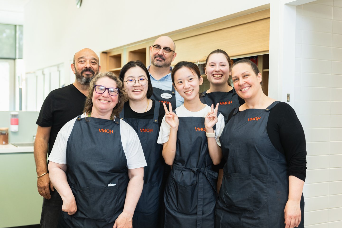 A group of seven people wearing navy aprons smiling at the camera